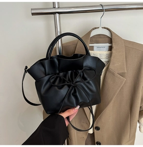 Close-up of black pleated cloud bag featuring large bow drawstring and smooth faux leather