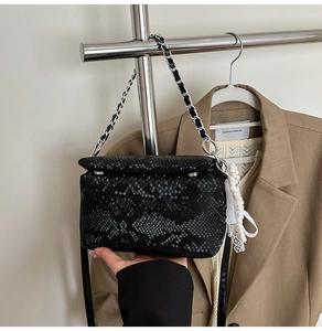 Detail of black snake pattern handbag with silver chain and pearl lace decorative charms