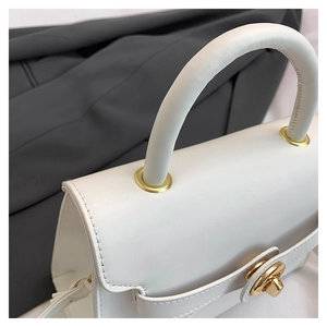 Close-up of white crossbody bag with gold metal twist lock and refined stitching