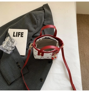 Détail du sac seau à motif cerise avec lanières en cuir rouge et pendentif cerise