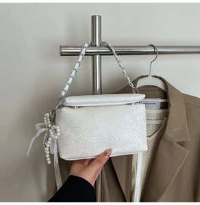 Close-up of white embossed crossbody bag with silver chain and pearl bow pendant