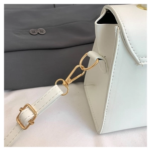 Detailed view of white leather crossbody bag with gold lobster clasp and adjustable strap