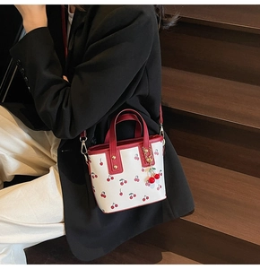 Détail du sac cabas blanc à imprimé cerises avec poignées et un pendentif mignon