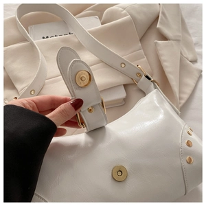 Gros plan d'un sac à bandoulière blanc brillant avec rivets dorés et texture cuir plissé