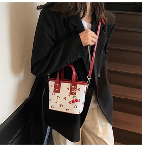 Détail d'un sac seau à imprimé cerise blanc avec poignées rouges sur un escalier