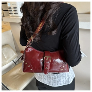 Détail du sac baguette bordeaux brillant avec rivets dorés et boucle décorative