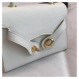 Close-up of elegant white leather bag with gold circular buckle and metal hardware