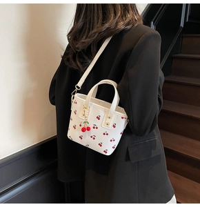 Vue détaillée du sac cabas blanc à motif cerise avec finitions dorées et charm cerise