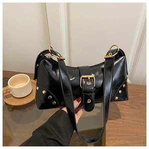 Gros plan sur un sac d'épaule en cuir verni noir avec boucles dorées et rivets