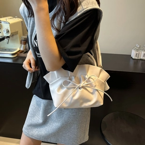 Chic white pleated cloud shoulder bag with leather bow detail in an elegant cafe setting