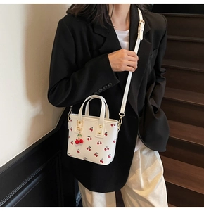 Détail du sac cabas blanc à motif cerises avec pendentif cerise rouge et boucles dorées