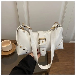 Détail du sac à bandoulière blanc avec rivets dorés et boucle sur une table en bois