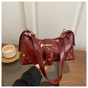 Détail d'un sac à bandoulière en cuir verni bordeaux avec boucles et rivets dorés