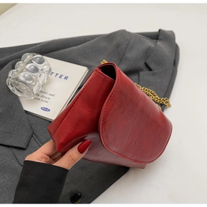 Detail of red oil-wax leather shoulder bag with gold chain strap on grey blazer