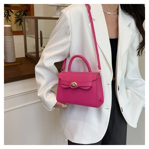 Close-up of magenta crossbody bag with golden knob clasp on white blazer outfit