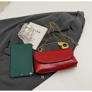 Detail of red wax leather crossbody bag with oversized gold safety pin handle and chain