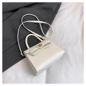 Detail of off-white leather handbag featuring a gold turn-lock and adjustable shoulder strap