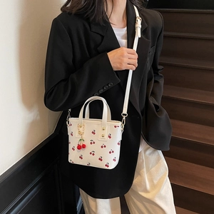 Sac fourre-tout blanc à motif cerise avec bandoulière et pendentif cerise porté par modèle