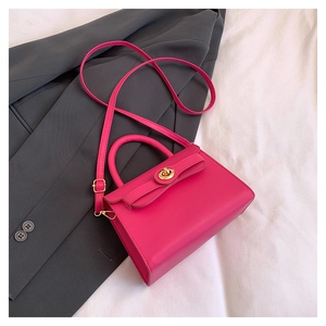 Close-up of rose red handbag with gold clasp on grey blazer and white bedding