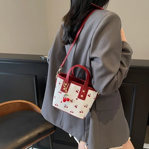 Femme portant un sac cabas blanc à motif cerises avec anses rouges et breloque cerise