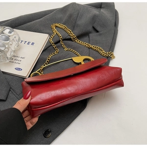 Detail of red leather shoulder bag with stylish gold safety pin buckle and metal chain strap
