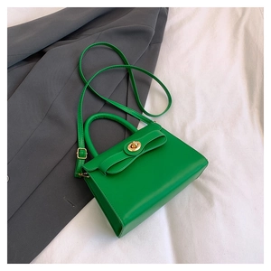 Detail of bright green leather handbag featuring a golden clasp and elegant bow ornament