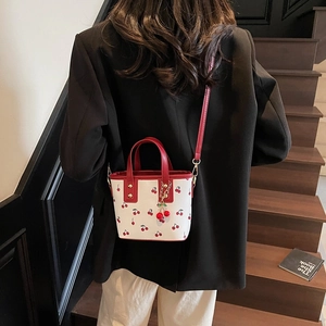 Sac seau blanc à imprimé cerise avec poignées rouges porté en bandoulière stylée