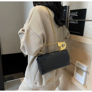 Detail of black patent leather shoulder bag with creative gold paperclip handle and chain