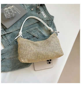 Flat lay of a woven straw tote bag with white leather handle on a blue denim jacket
