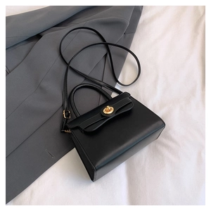 Detailed view of black trapezoid crossbody bag with a round gold metallic clasp