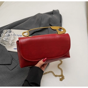 Detail of red crossbody bag featuring gold safety pin handle and chain strap on blazer background