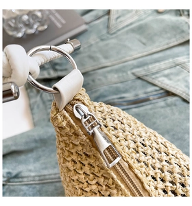 Detail of silver zipper and hardware on beige woven straw tote bag over denim fabric