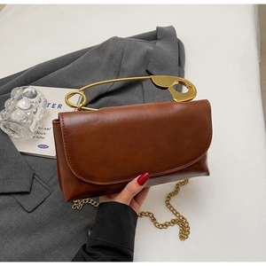 Detail of a brown vintage leather handbag featuring a unique gold safety pin handle and chain