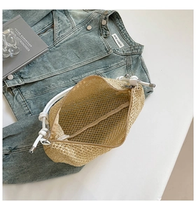 Detail of beige woven straw tote bag featuring white leather handles and zip closure