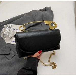 Detailed view of black glossy leather handbag with creative golden paperclip handle