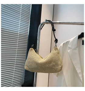 Detail of a beige woven straw hobo bag with black knotted shoulder strap and crescent shape