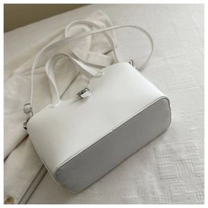 Detail view of white minimalist bucket bag with metal twist lock and thin strap