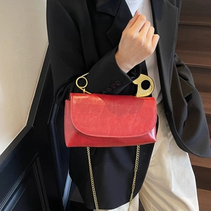 Red crossbody bag with unique gold paperclip handle and metal chain strap worn on model