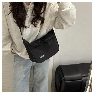 Detail of minimalist black nylon crossbody bag featuring a woven strap and logo patch
