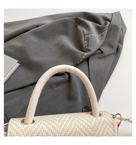 Detailed close-up of woven texture and beige leather handle on stylish square crossbody bag