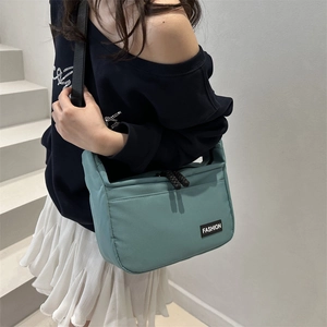Minimalist cyan nylon tote bag with black strap shown in a stylish street style view