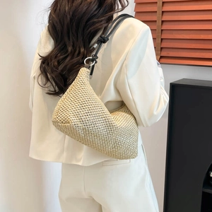 Beige woven straw tote bag with black leather shoulder strap on a model in white suit