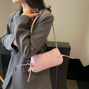 Pink patent leather underarm bag with bow details and studs worn by a model