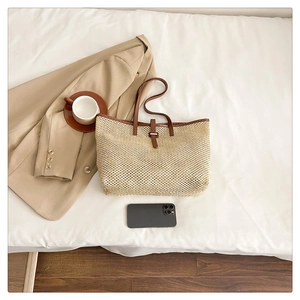 Top view of large straw tote bag with brown leather straps and buckle on white bedding