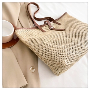 Detail of hand-woven straw tote with brown PU leather straps and metal buckle adjustment
