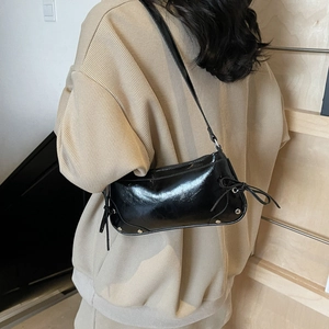 Black glossy underarm bag with bow ribbons and rivets shown on a model's shoulder