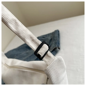 Detail of white corduroy bag showing adjustable strap buckle and zipper closure