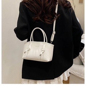 Dettaglio borsa beige con scritta fashion e manico con nodo metallico indossata da una modella