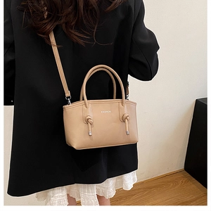Dettaglio borsa a mano in pelle beige con testo Fashion e decoro manico a nodo
