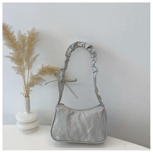 Détail macro du sac à bandoulière argenté métallisé avec nœud élégant et sangle à volants